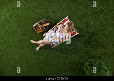 Una donna seduta al sole su un prato in un parco con un cestino da pic nic, vista aerea Foto Stock