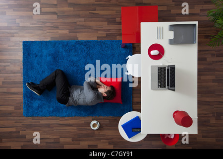 Un imprenditore di dormire su un tappeto vicino alla sua scrivania, vista aerea Foto Stock