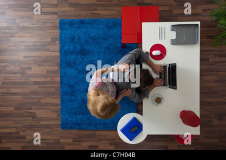 Una donna in piedi dietro il suo uomo mentre lavora nel suo ufficio di casa, vista aerea Foto Stock