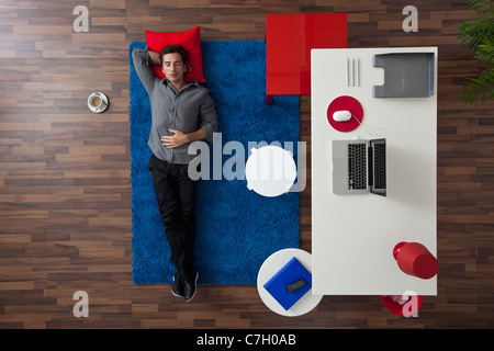 Un uomo disteso su un tappeto accanto a casa sua scrivania da ufficio, vista aerea Foto Stock