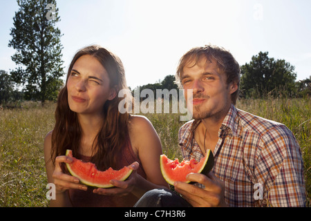 Giovane seduto a mangiare il melone in campo Foto Stock