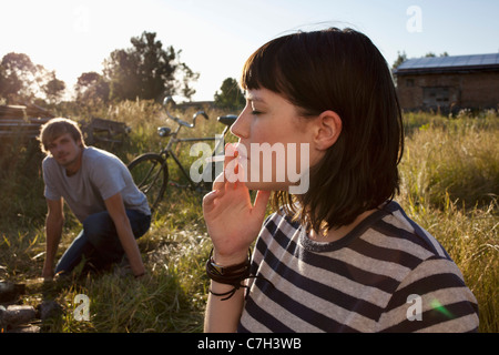 Ragazza di fumare in campo come ragazzo in orologi di sfondo Foto Stock