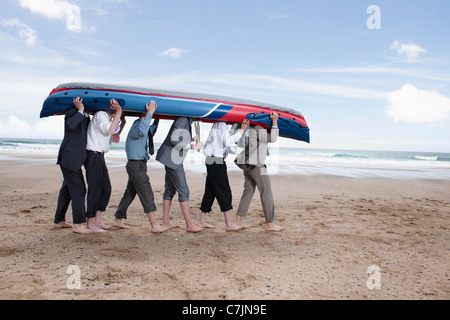 Imprenditori che trasportano Canoe sulla spiaggia Foto Stock