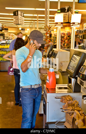 Mentre si effettua un acquisto di supermercati, un giovane ispanico scansioni adulto sconto di un codice a barre coupon in un self-checkout kiosk. Foto Stock