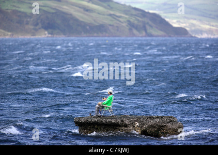 Un manichino vestito come un pescatore sorge su un promontorio roccioso nel mare d' Irlanda nei pressi del villaggio di Waterfoot, sulla contea di Antrim Foto Stock