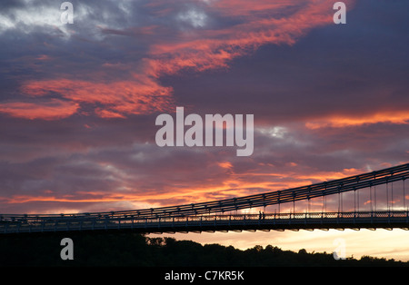 Due stagliano figure camminare sopra il ponte sospeso di Clifton a Bristol al tramonto Foto Stock