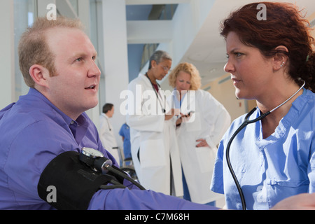 Infermiera femmina la misurazione di una pressione del sangue del paziente con i suoi colleghi in background Foto Stock