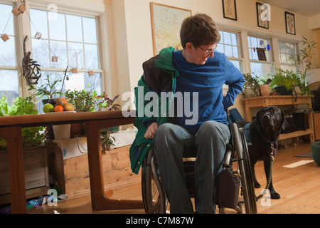 Donna con sclerosi multipla in una sedia a rotelle messa sul suo cappotto con servizio cane osservando il suo Foto Stock