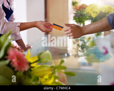 Giovane donna che lavora come un fioraio dando la carta di credito al cliente dopo l'acquisto. Sagoma orizzontale, primo piano Foto Stock