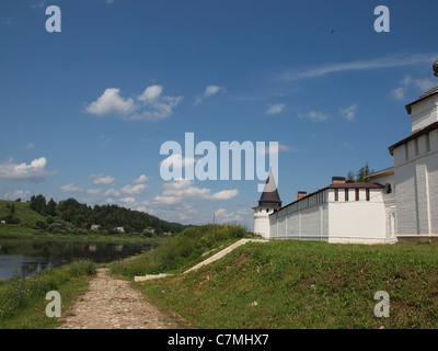 La strada lastricata di pietra la circonda un edificio di mattoni bianchi in piedi sulla riva del fiume. Foto Stock