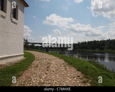 La strada lastricata di pietra la circonda un edificio di mattoni bianchi in piedi sulla riva del fiume. Foto Stock