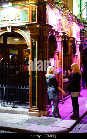 2 ragazze fuori Dublino pub di fumare durante la notte Foto Stock