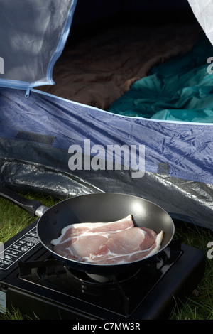 La frittura di bacon su un piccolo portatile fornello a gas nella parte anteriore di un porta tenda Foto Stock