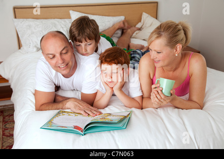 Famiglia di quattro lettura a letto insieme Foto Stock