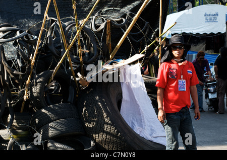 Guardia di sicurezza camicia rossa di fronte alla barricata / checkpoint fatto di pneumatici, filo di bob e pali di bambù affilati, Bangkok, Thailandia. © Kraig Lieb Foto Stock