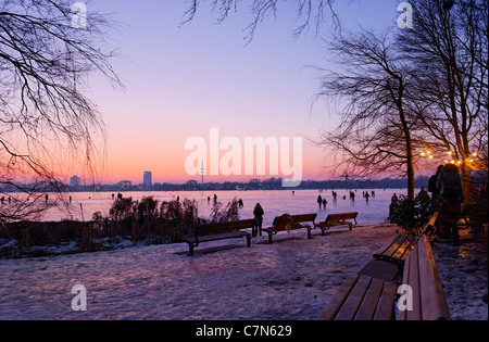 Saldamente Aussenalster congelato, Esterno lago Alster, dopo il tramonto, persone, divertimenti, ghiaccio, neve, in inverno, Amburgo, Germania Foto Stock