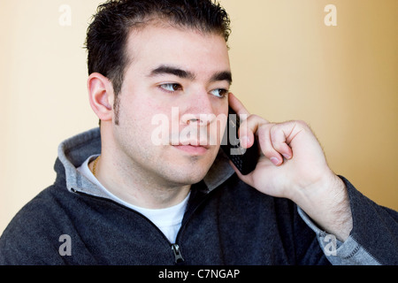 Un giovane uomo che parla sul suo telefono cellulare. Egli sta tenendo il telefono con la sua mano destra ma ascolto con il suo orecchio sinistro. Foto Stock