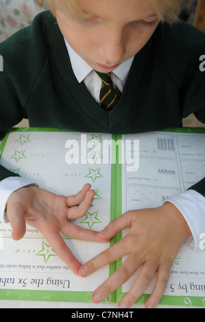 Bionda boy in verde uniforme scolastica conta sulle sue dita facendo il suo dovere di matematica cercando di aggiungere fino somme seduti al tavolo da pranzo Foto Stock