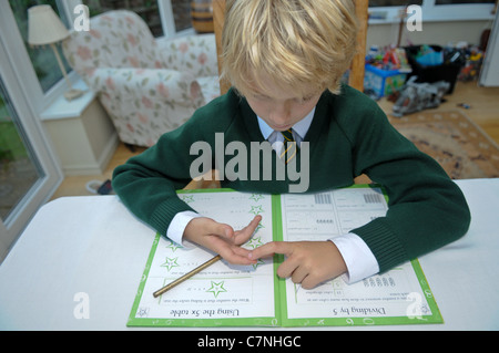Bionda boy in verde uniforme scolastica conta sulle sue dita facendo il suo dovere di matematica cercando di aggiungere fino somme seduti al tavolo da pranzo Foto Stock