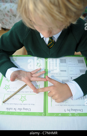 Bionda boy in verde uniforme scolastica conta sulle sue dita facendo il suo dovere di matematica cercando di aggiungere fino somme seduti al tavolo da pranzo Foto Stock
