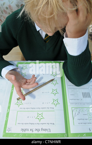 Bionda boy in verde uniforme scolastica conta sulle sue dita facendo il suo dovere di matematica cercando di aggiungere fino somme seduti al tavolo da pranzo Foto Stock