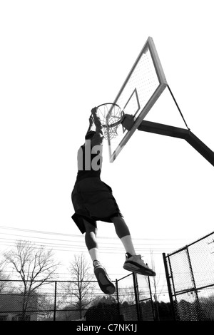 Un giocatore di basket appesi al cerchione dopo slam dunking la sfera in bianco e nero. Foto Stock