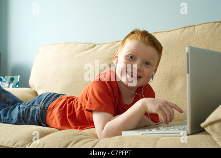 Ragazzo in cuffie utilizzando laptop sul lettino Foto Stock