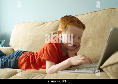 Ragazzo in cuffie utilizzando laptop sul lettino Foto Stock