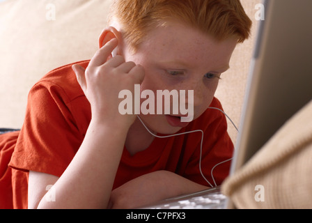 Ragazzo in cuffie utilizzando laptop sul lettino Foto Stock