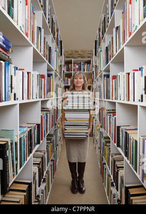 Donna anziana il trasporto di libri in biblioteca Foto Stock