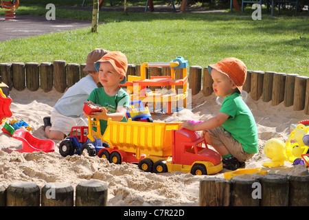 I bambini giocando in una buca di sabbia con giocattoli Foto Stock