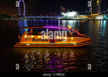 Imbarcazione turistica illuminata di notte sul Fiume Singapore con il flyer in background Foto Stock