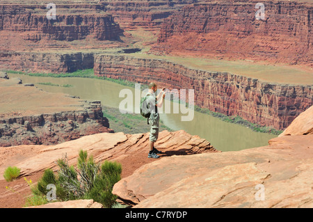 Un escursionista smette di prendere una fotografia di formazioni rocciose scolpite dal fiume Colorado in Dead Horse Point State Park, Utah Foto Stock