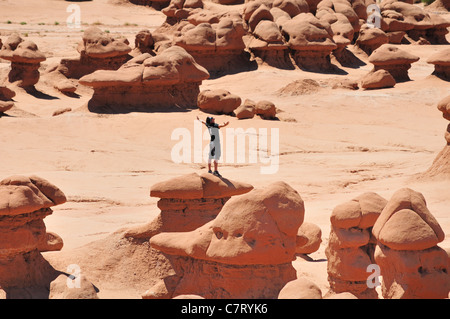 Un giovane che abbraccia il cielo come egli si trova in cima ad una formazione rocciosa in Goblin Valley State Park, Utah Foto Stock