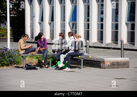 Un gruppo di giovani donne seduti sui banchi all'esterno dell'edificio Foto Stock