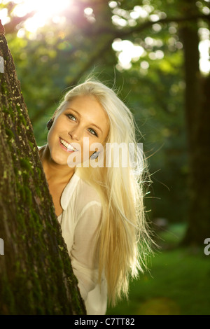 Naturale bellezza giovani nascondersi dietro a un albero. Sole splende. Foto Stock