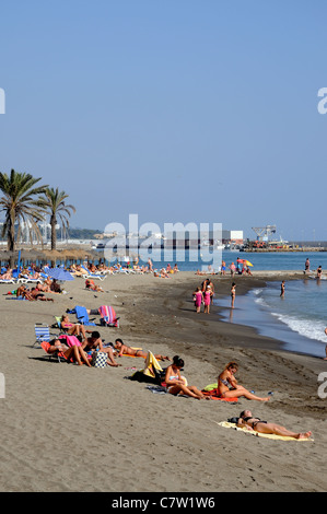 I turisti sulla spiaggia vicino al porto peschereccio, Marbella, Costa del Sol, provincia di Malaga, Andalusia, Spagna, Europa occidentale. Foto Stock