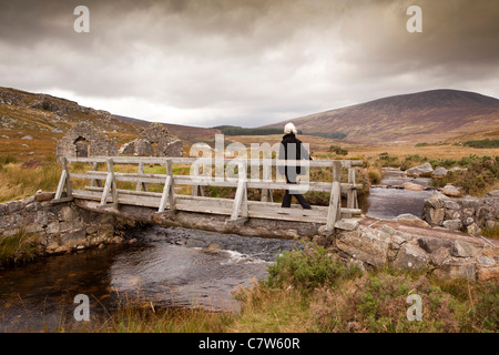 Irlanda, Co Wicklow, Wicklow Mountains visitatore attraversando Avonmore River bridge al vecchio rovinato granite house Foto Stock