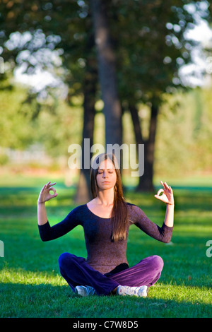 Una giovane donna in posizione di yoga, bracci sollevati, in un giardino Foto Stock