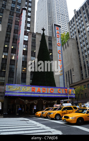 Quattro giallo taxi in attesa in corrispondenza di una striscia whitre attraversamento pedonale davanti al neon rosso della Radio City Music Hall, 6th Avenue, New York City Foto Stock