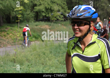 La donna-ciclista in un blu scuro casco e occhiali neri sorrisi Foto Stock