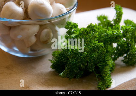 I funghi in una ciotola di vetro prezzemolo su una tavola di legno annoiato pronto per cucinare Foto Stock