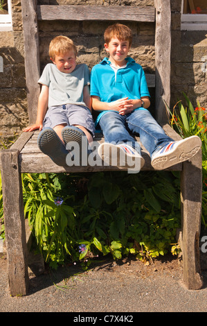 Due ragazzi seduti sulla sedia gigante al di fuori della vecchia scuola negozio di artigianato a Muker in Swaledale nel North Yorkshire , Inghilterra , Regno Unito Foto Stock