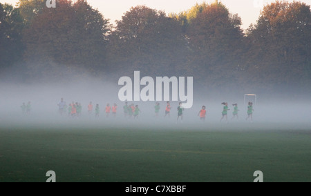 La scuola dei bambini in esecuzione su foschia mattutina, Wandsworth Common, Londra UK Foto Stock