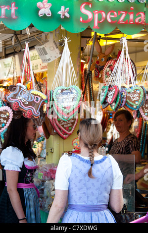 Le giovani ragazze nel tradizionale costume tedesco (Dirndl) sta per acquistare un tradizionale Gingerbread cuore al Cannstatter Wasen Foto Stock