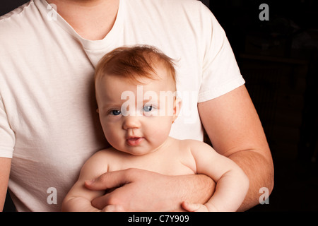 Padre in maglia bianca tenendo neonato su sfondo nero Foto Stock