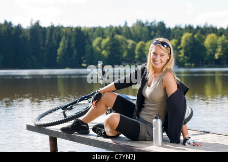 Sport Bike giovane donna seduta sul molo dal lago naturale Foto Stock