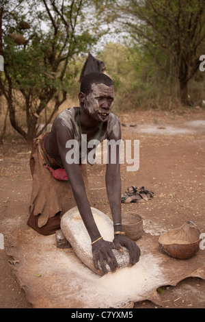 Mursi donna fare farina di granturco sul vecchio mulino in pietra, Jinka, Valle dell'Omo, Etiopia, Africa Foto Stock