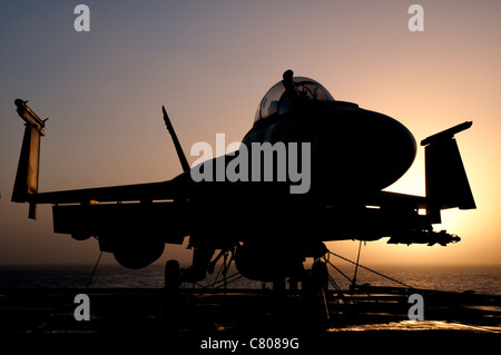 Silhouette di un US Navy F/A-18E Super Hornet parcheggiata sul ponte di volo della portaerei USS Nimitz al largo delle coste del Pakistan. Foto Stock