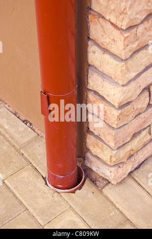 Rosso di canalizzazione delle acque piovane di stagno su angolo della casa fatta di mattoni decorativi. Foto Stock
